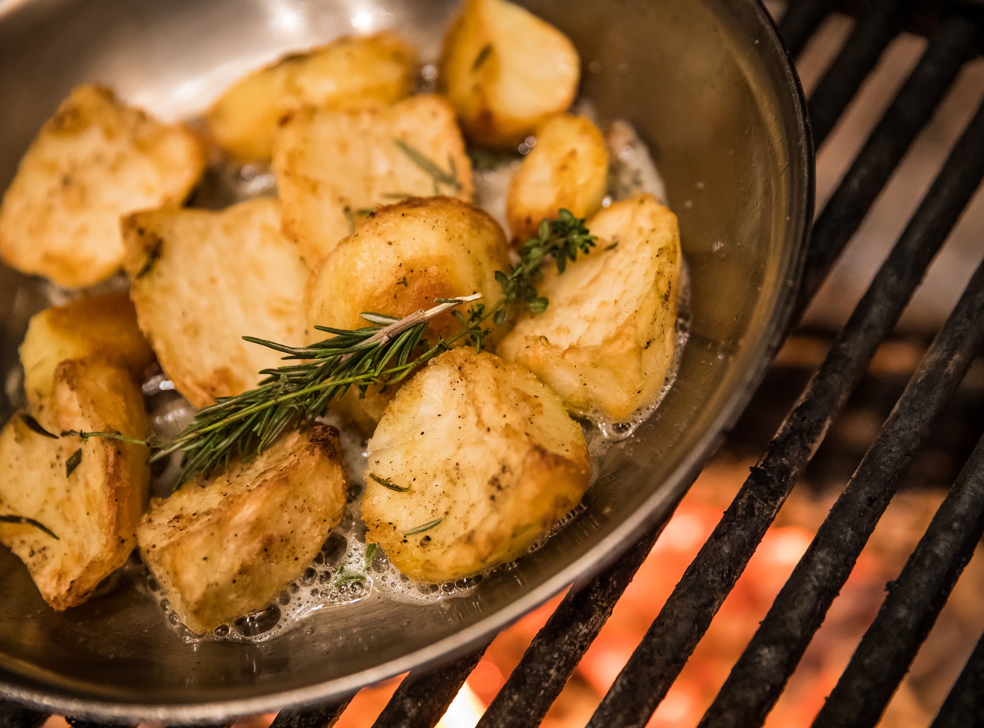 Close up of pan roasting potatoes over fire